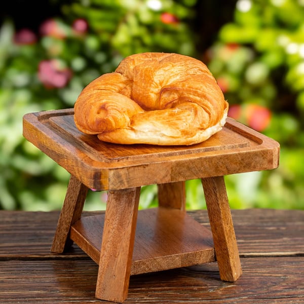 Golden-brown croissant on a small wooden stand, with a blurred green garden background.