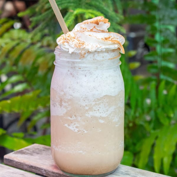 A creamy blended drink with whipped cream and cinnamon in a mason jar on a wooden surface.