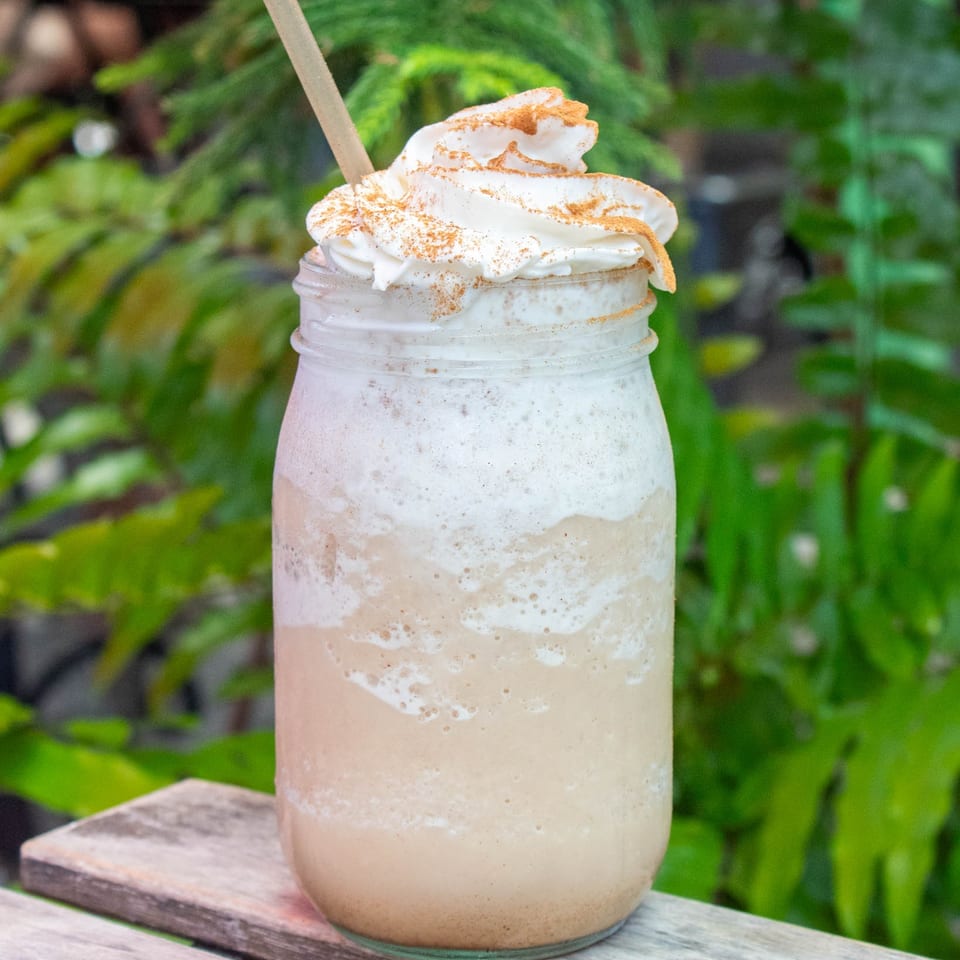 A creamy blended drink with whipped cream and cinnamon in a mason jar on a wooden surface.
