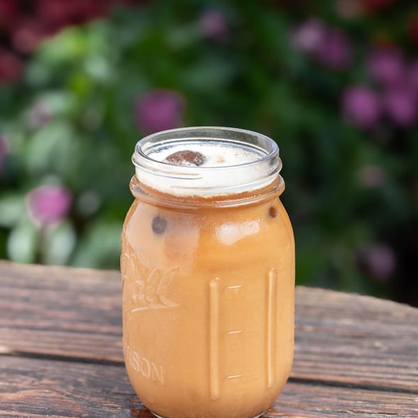Iced coffee in a mason jar with foam and a chocolate-covered coffee bean on a wooden table.