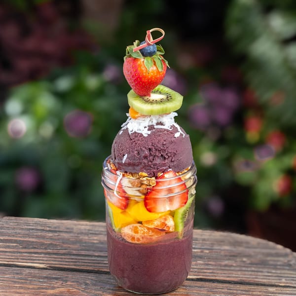 A vibrant acai bowl in a glass jar, topped with fresh fruit, granola, and coconut flakes.
