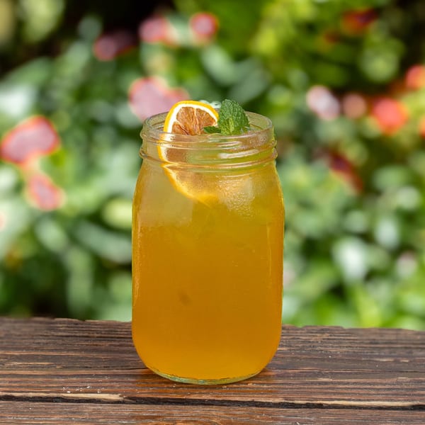 Iced tea in a mason jar with a lemon slice and mint sprig on a wooden table.
