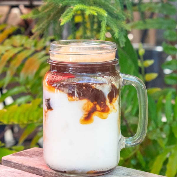 Iced coffee with milk and chocolate syrup in a mason jar on a wooden table.