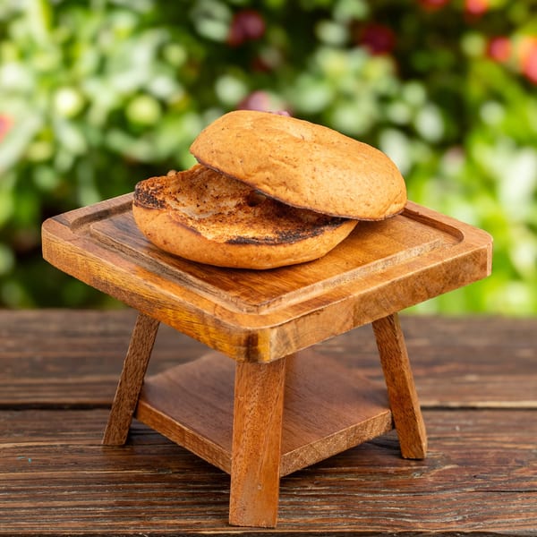 Toasted burger bun halves on a small wooden serving stand, with a blurred green background.