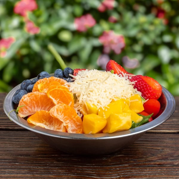 A colorful fruit salad with blueberries, tangerines, mango, strawberries, and shredded cheese in a metal bowl.