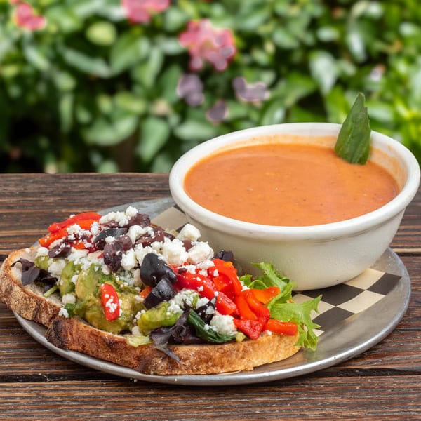 Avocado toast with feta, olives, and red peppers, served with a bowl of tomato soup.