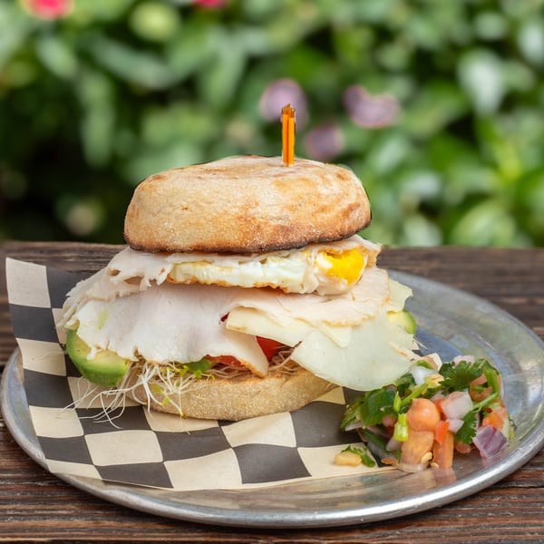 Breakfast sandwich with turkey, egg, avocado, sprouts, and salsa on a metal plate.