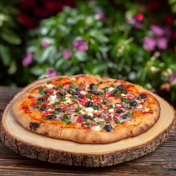 A freshly baked pizza with olives, red peppers, feta, and green onions on a wooden board.