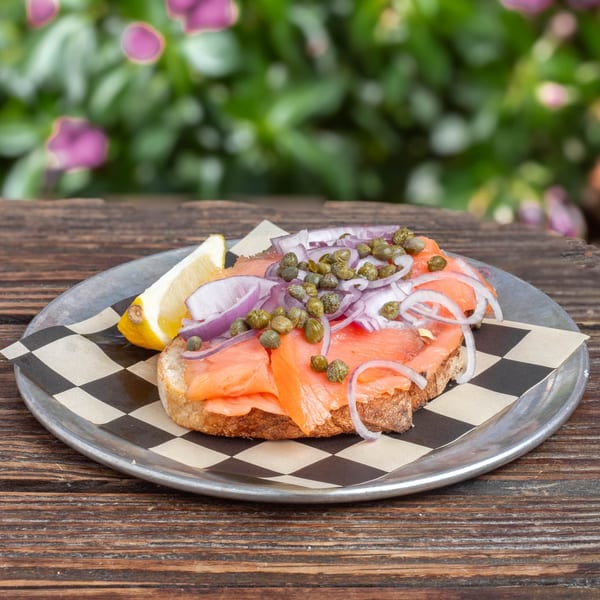 Smoked salmon toast with red onions, capers, and a lemon wedge on a metal plate.
