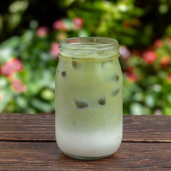 Iced matcha latte in a mason jar on a wooden table with a blurred green and pink floral background.